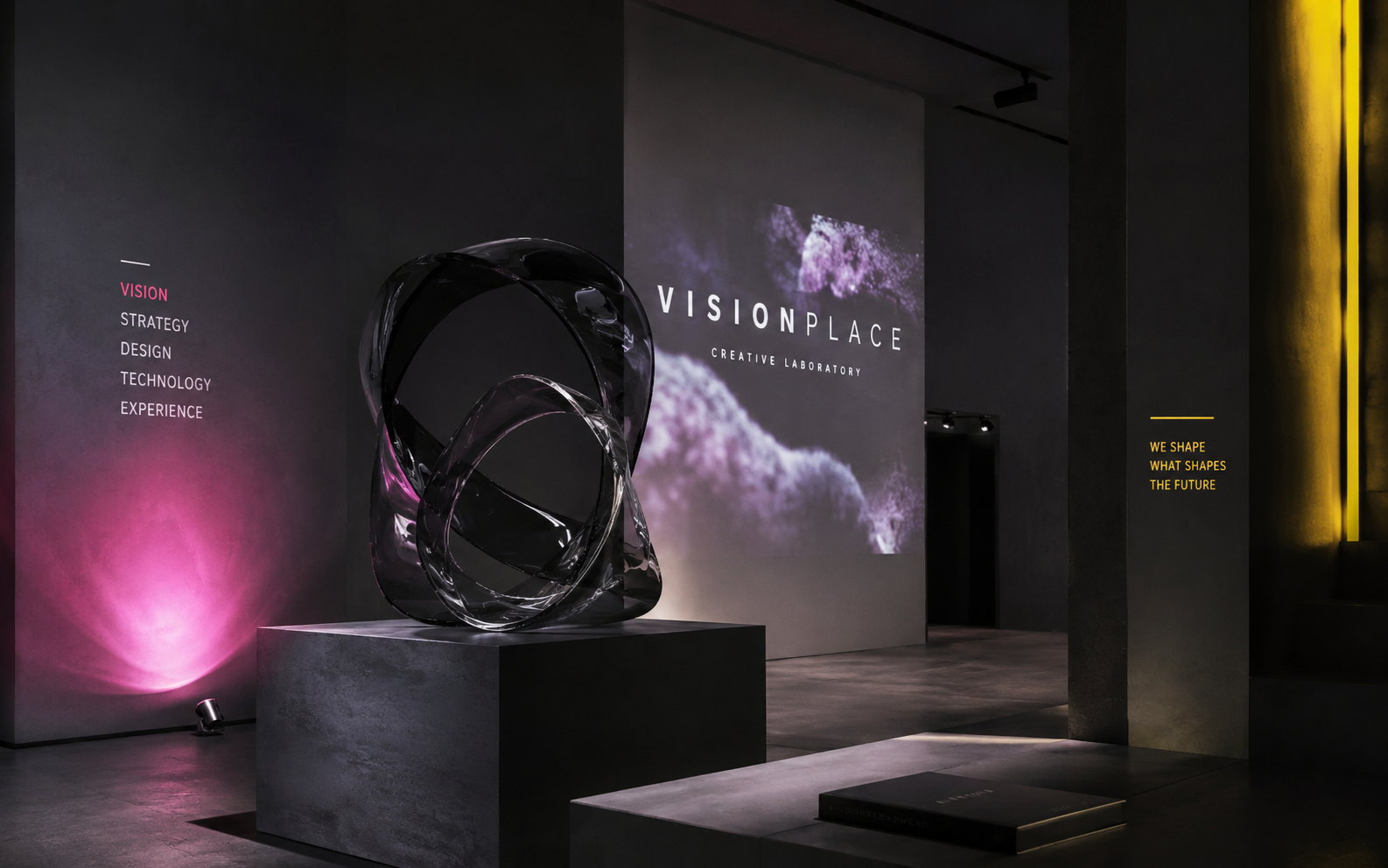 Immersive VISIONPLACE creative gallery with a sculptural glass form, projected identity graphics and dramatic pink and yellow light